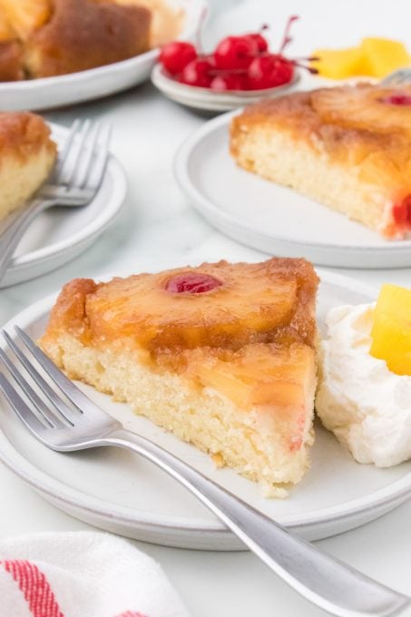 A slice of yellow cake with pineapple and cherries.