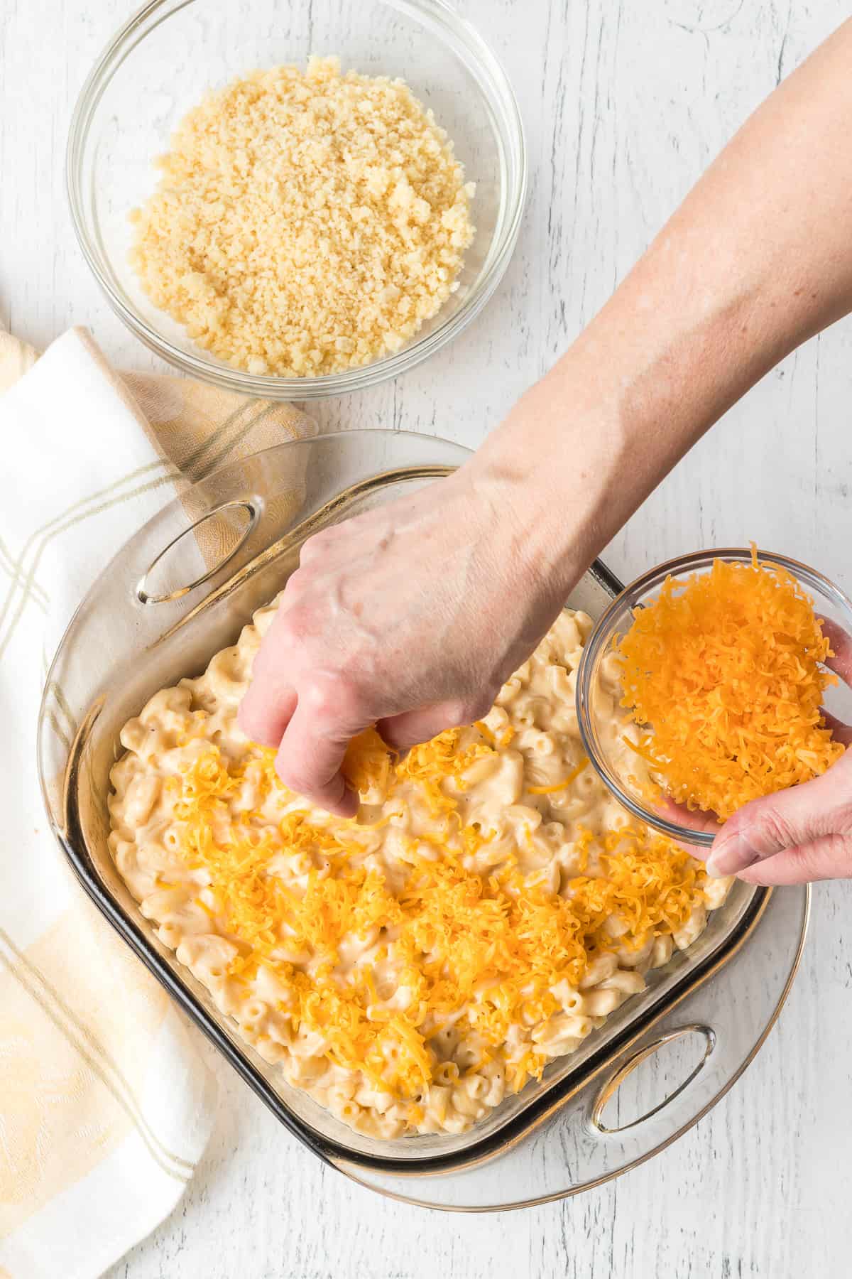 Putting cheese on top of a cheese and macaroni before going into the oven.