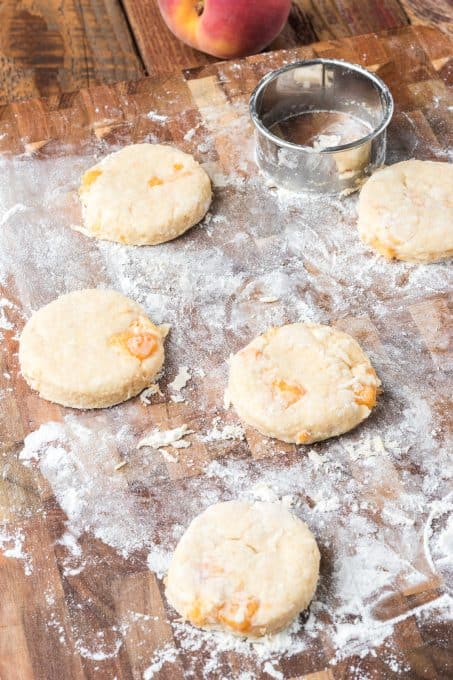 Scone dough on a floured board with pieces of peach inside.
