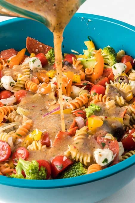 Pouring dressing over a pasta salad with Italian flavors.