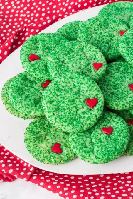 A plate of sugar cookies with green sprinkles and a red heart.