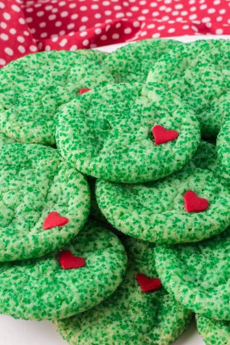 Sprinkled green sugar cookies with red candy hearts.