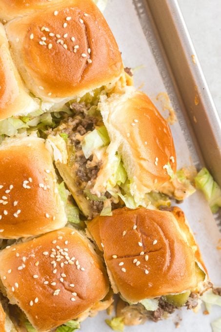 A slider with ground beef, lettuce, pickles, cheese and sauce.