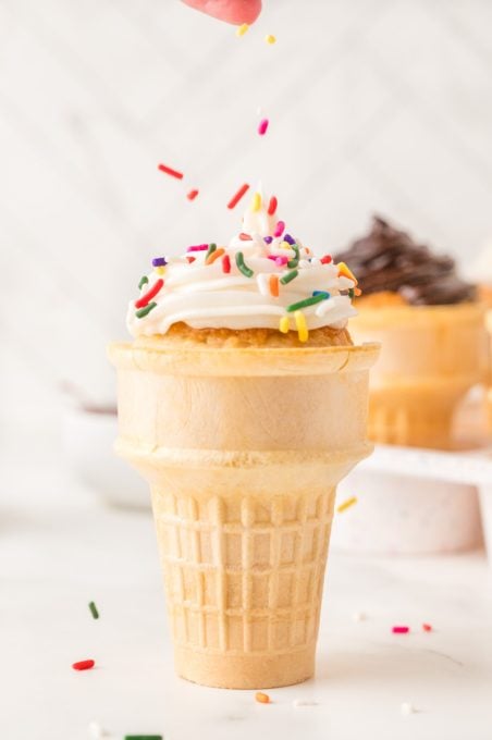 Putting sprinkles on a wafer cone cupcake.