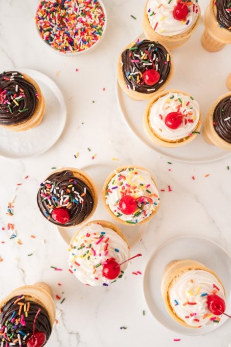 Frosting, sprinkles and cherries on cupcake cones.